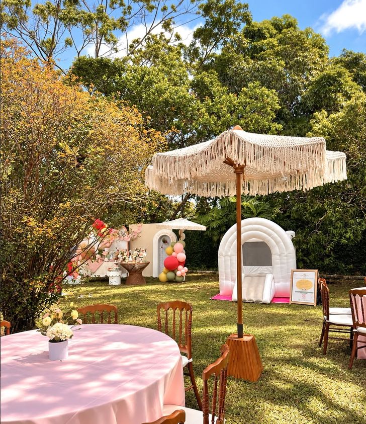 Festa no jardim com ombrelone de macramê, inflável arco-íris branco e mesa rosa