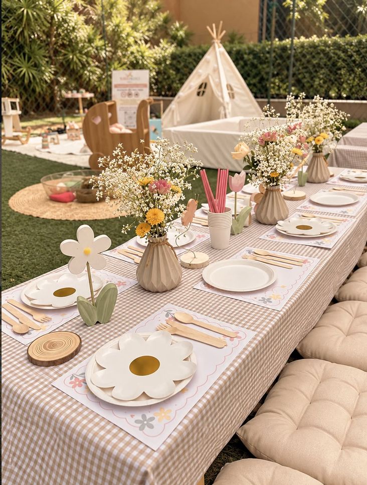 Mesa kids baixa com toalha xadrez, pratos de margarida e vasos de flores do campo